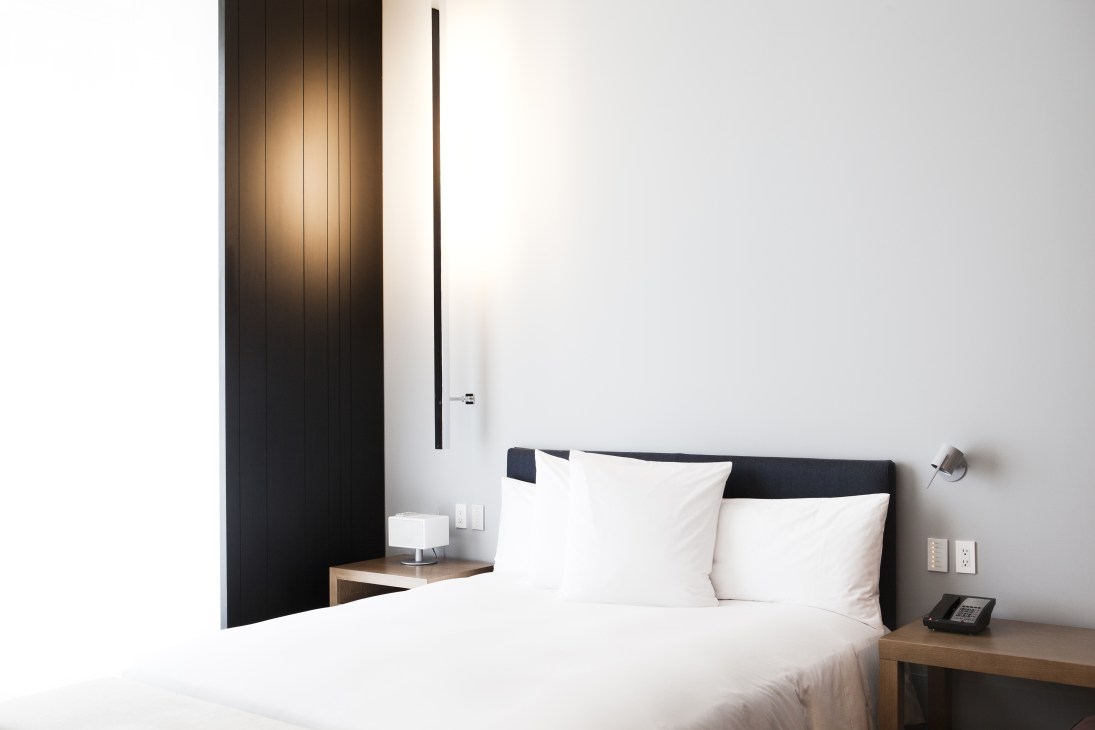 Minimalist hotel guest room with bed, dark wood accent wall, and bedside table at Andaz Fifth Avenue.
