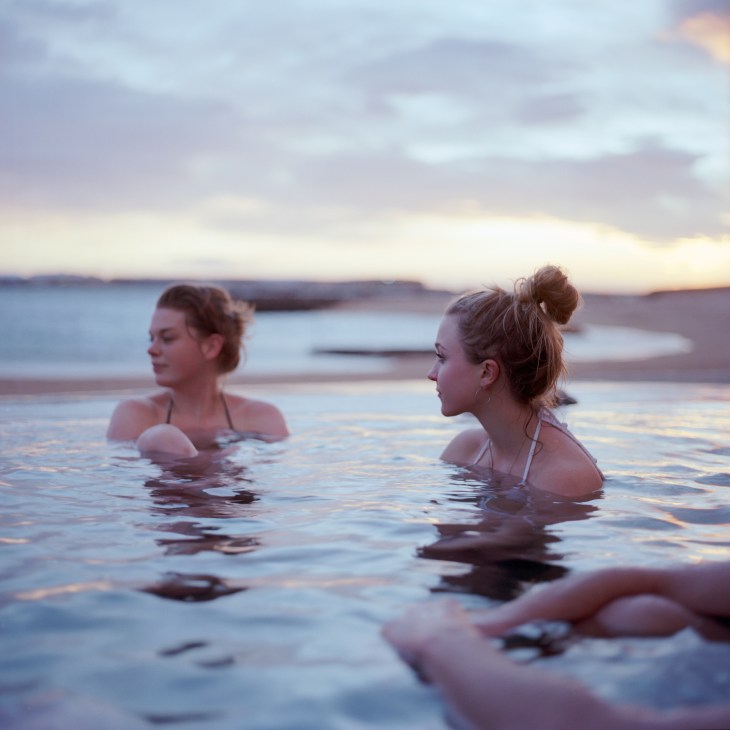 Two women bathing in steaming geothermal water at sunset at Ylstrondin Nautholsvik in Reykjavik, Iceland.
