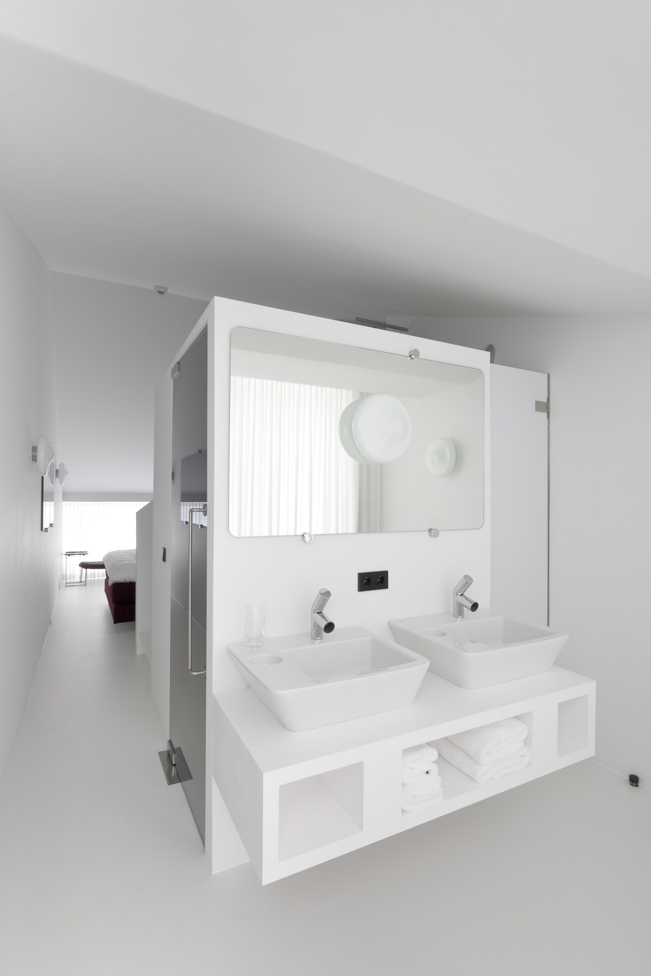Minimalist white bathroom with double sinks, large mirror and modern fixtures at Hotel Zenden.