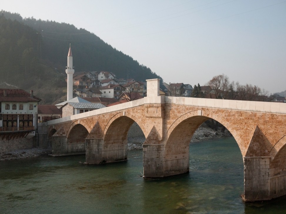 Stone bridge spanning turquoise river with mosque minaret and hillside buildings in Konjic, Bosnia.
