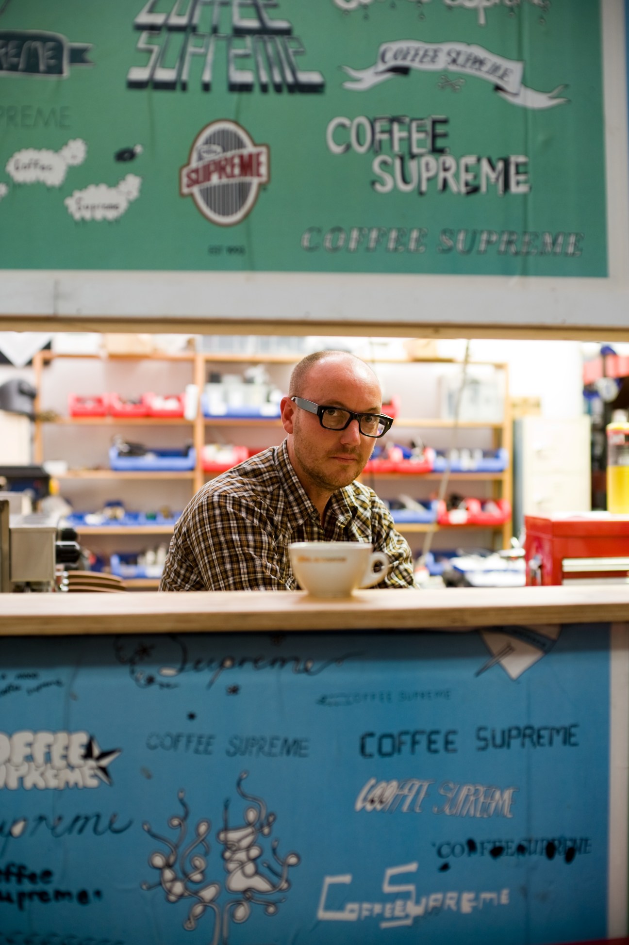 Al Keating stands behind the counter at Good One café with a Coffee Supreme branded wall behind him.