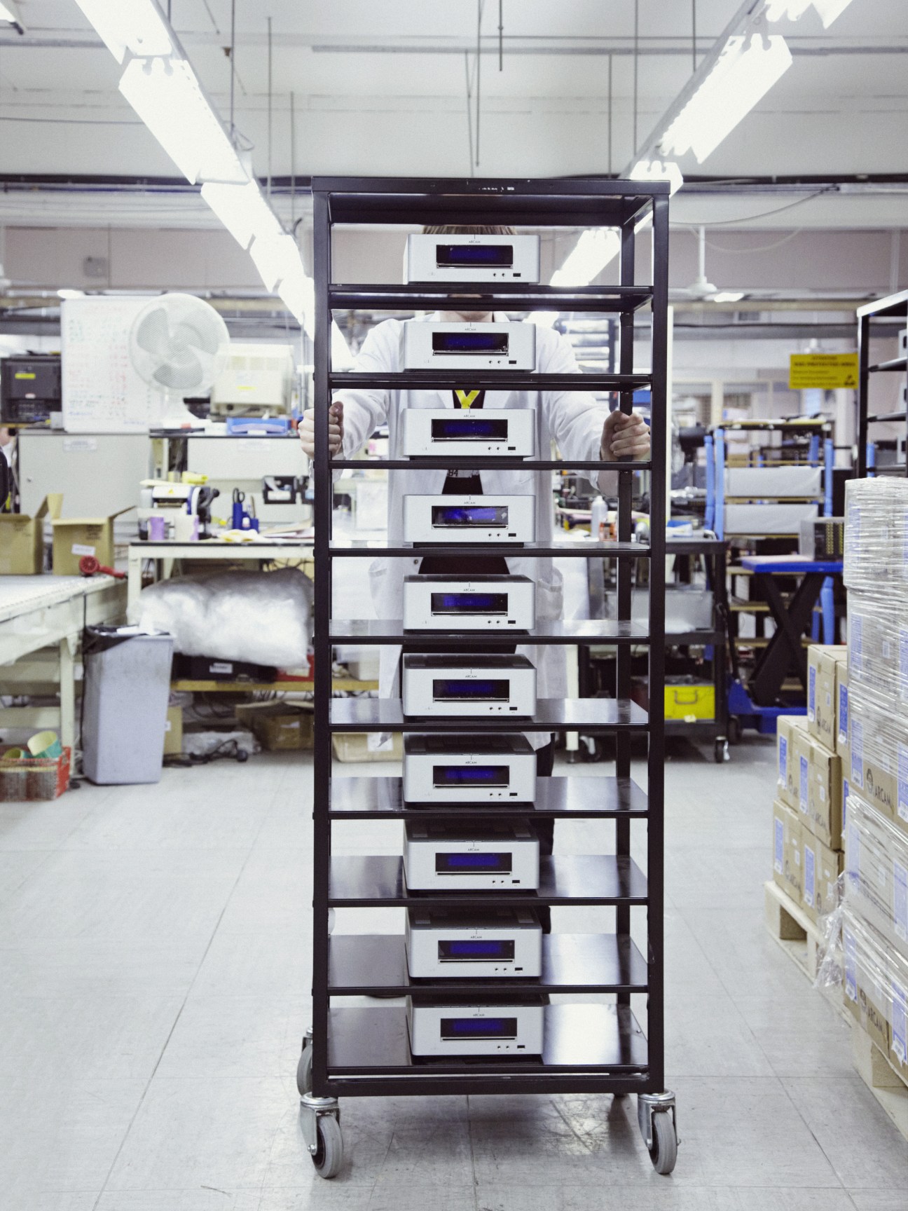 Stack of white Arcam audio receivers mounted on a black metal rack in a factory.