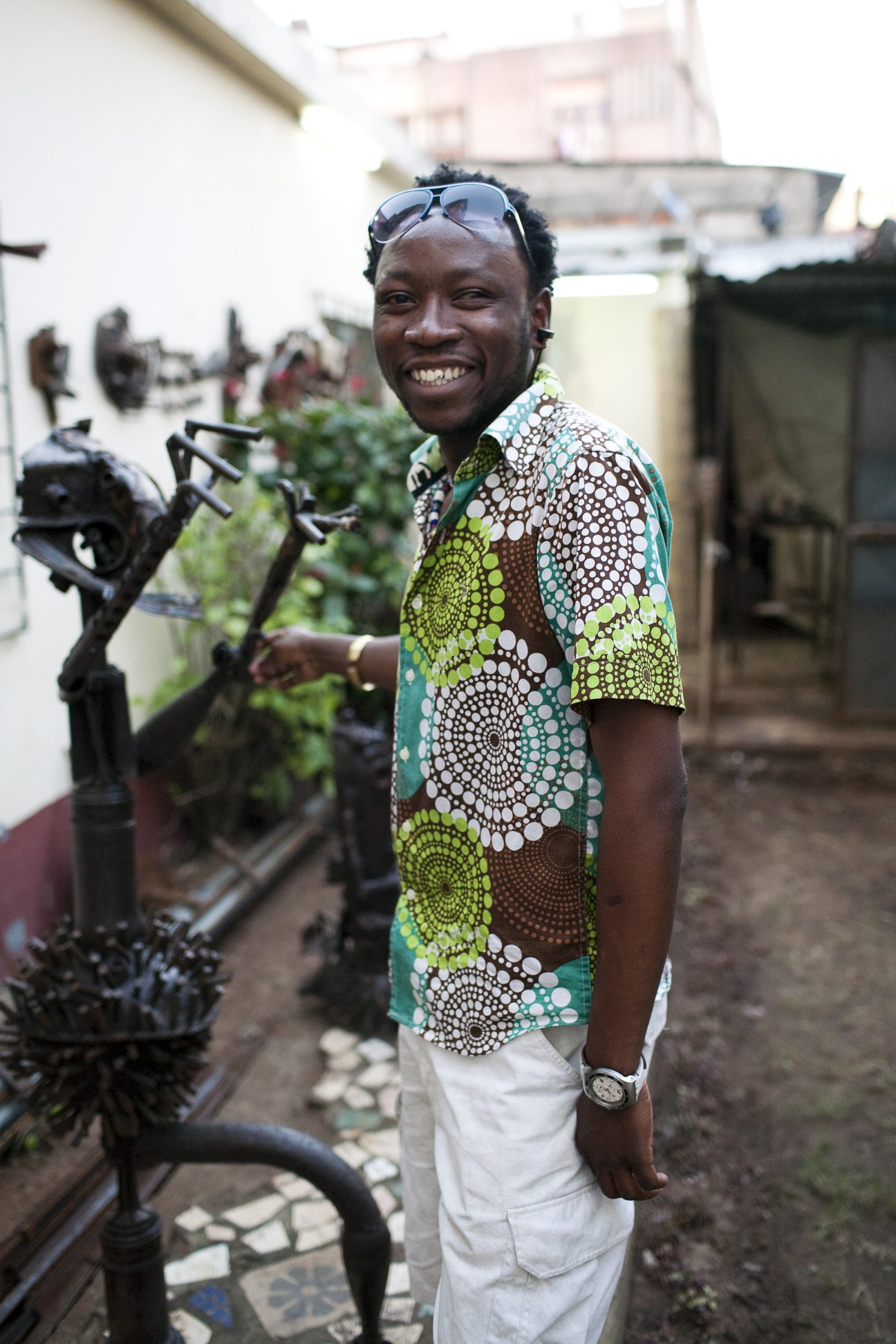 Artist Goncalo Mabunda smiling in his studio among metal sculptures made from civil war munitions.