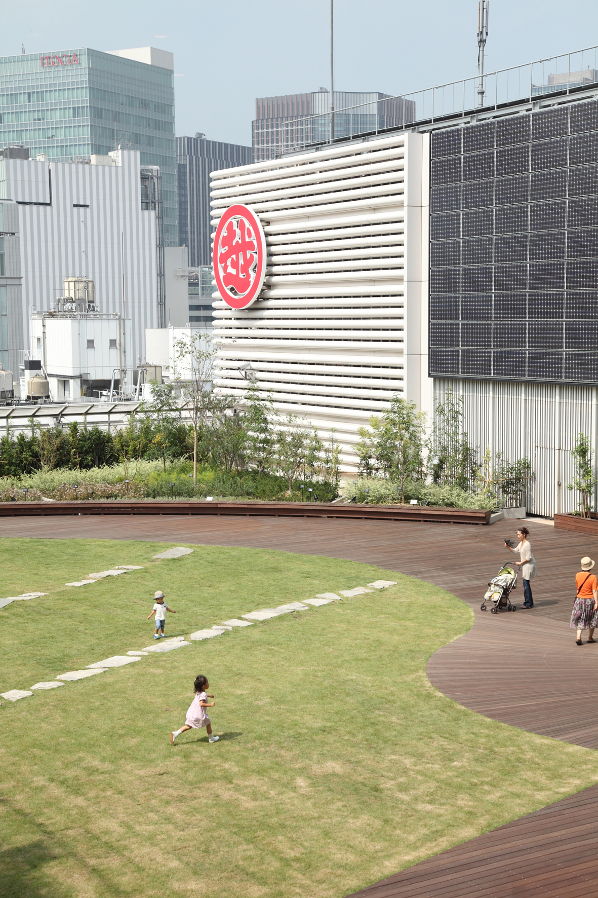 Mitsukoshi's Ginza terrace with lawn, wooden deck, and children playing near planted areas and Tokyo cityscape.