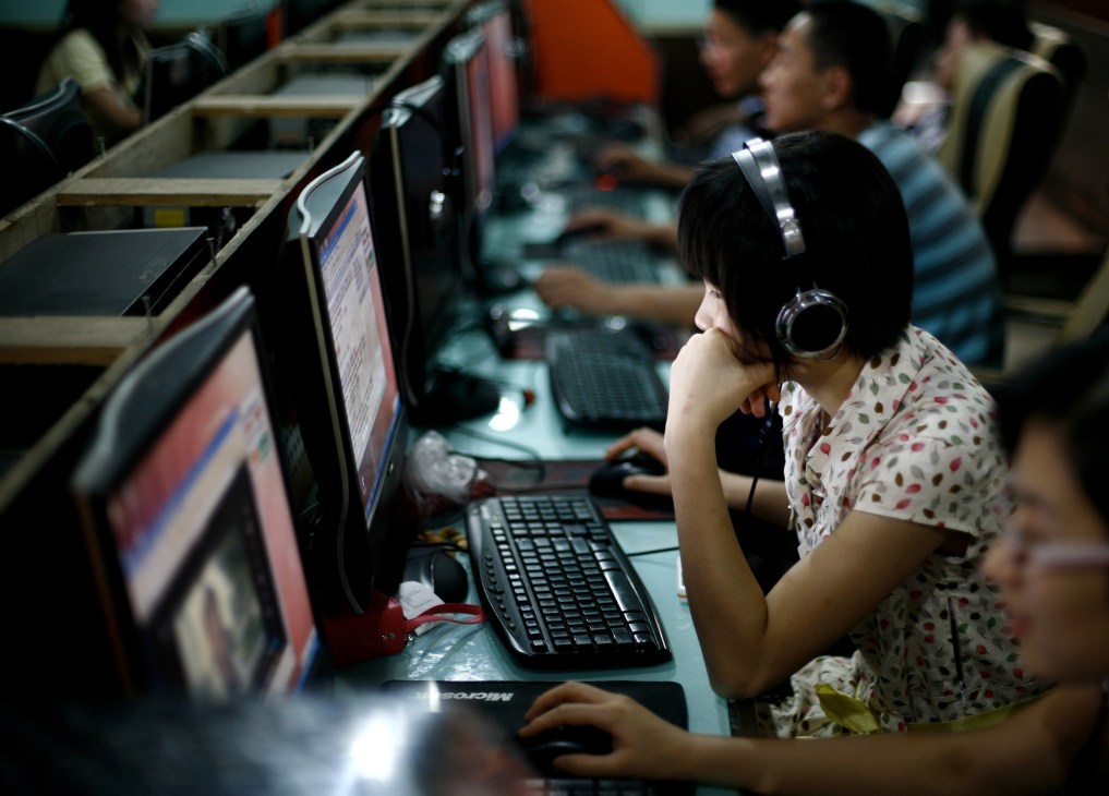 Young woman wearing headphones at computer in internet café with other users at terminals