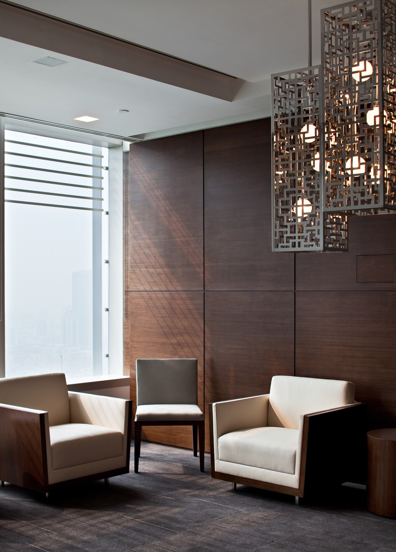 Modern office lounge with upholstered chairs, dark wood paneling, and decorative metal screen in HSBC Shanghai headquarters.
