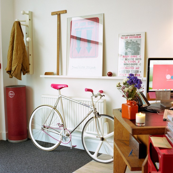 Not To Scale London office reception desk with vintage bicycle, coat rack, and framed artwork on white walls.