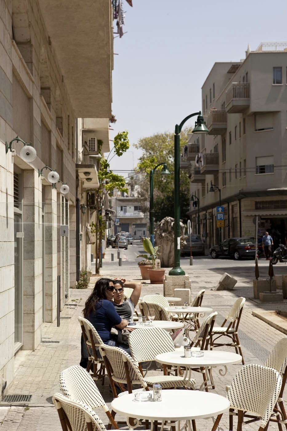 Two people seated at Cardo café and wine bar on a sunny Tel Aviv street lined with historic stone buildings.