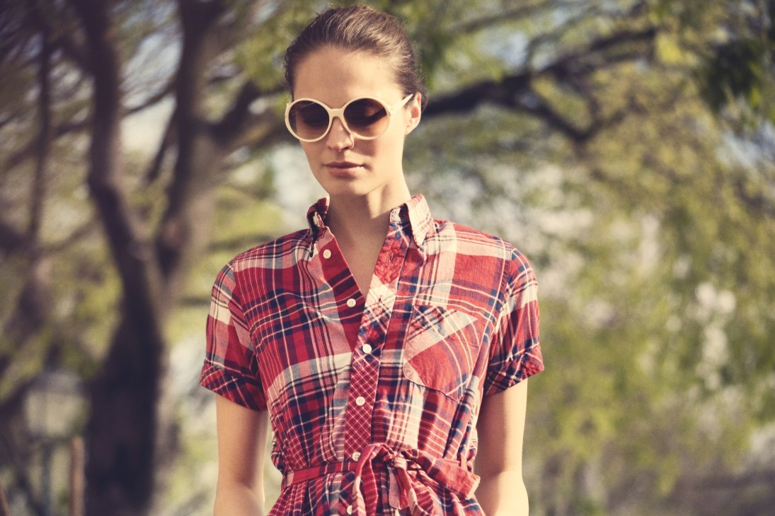Model wearing Roger Vivier sunglasses and FWK by Engineered Garments red plaid dress in a sunny outdoor setting.