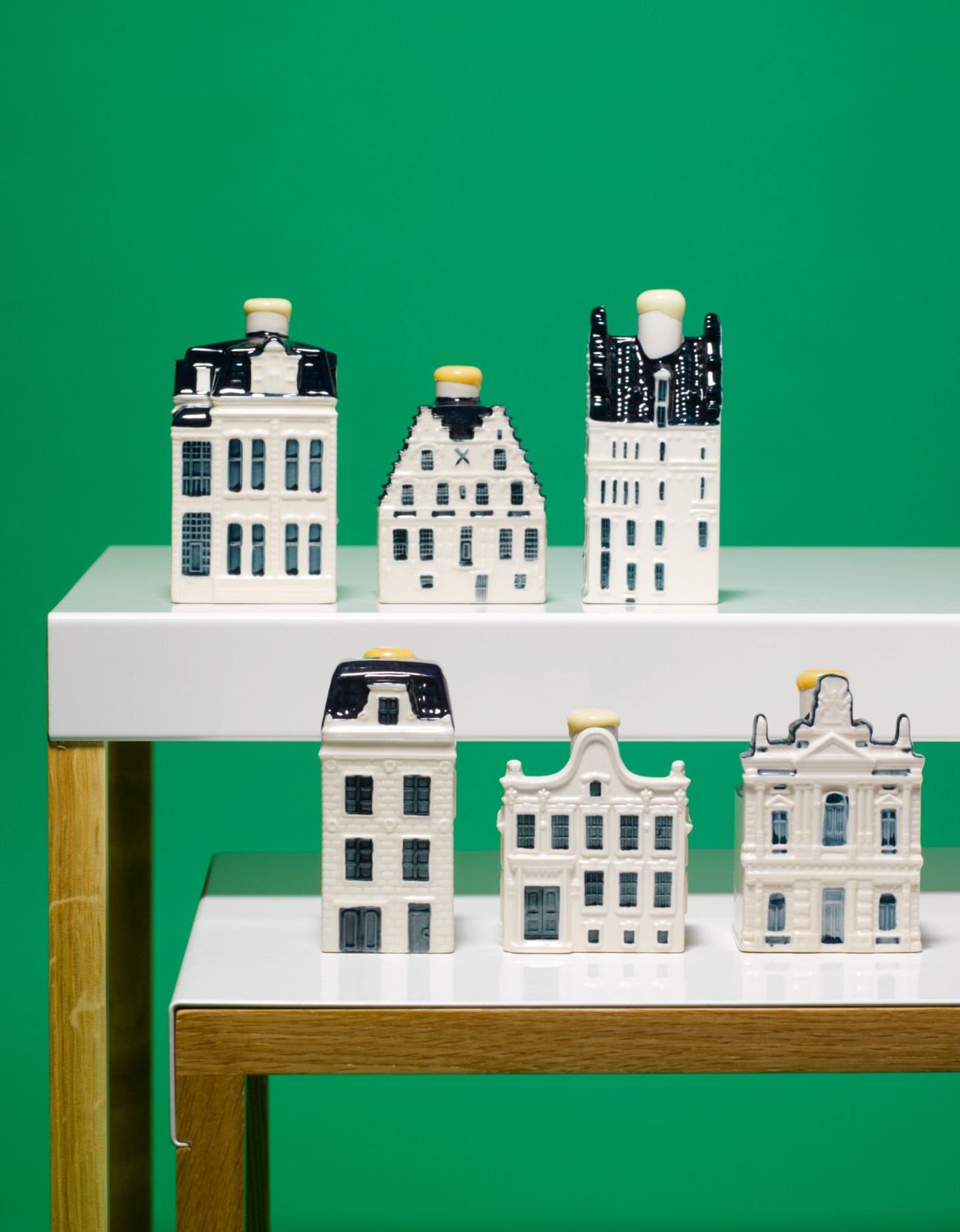 KLM Delft Blue ceramic houses with jenever, displayed on white shelves against a green background.