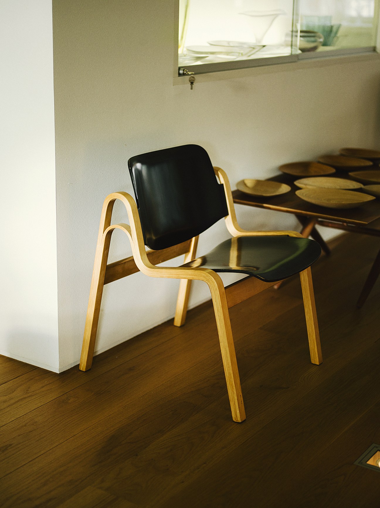 Wilhelmiina chair by Ilmari Tapiovaara with wooden frame and black leather seat in bright apartment.