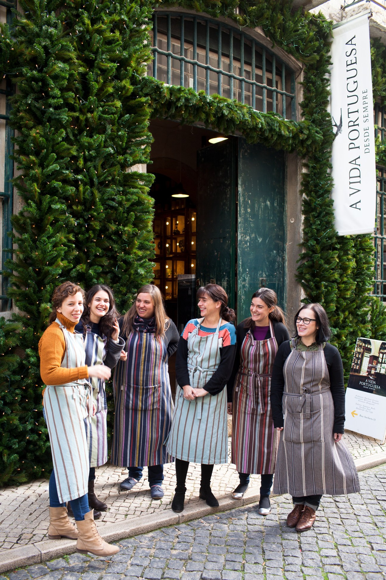 Six women stand outside A Vida Portuguesa storefront with ivy-covered walls and green door.