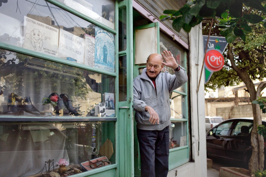 Sarkis Tekirian, an elderly Armenian cobbler, waves from the doorway of his shoe repair shop with a green storefront in Beirut's Mar Mikhael neighbourhood.