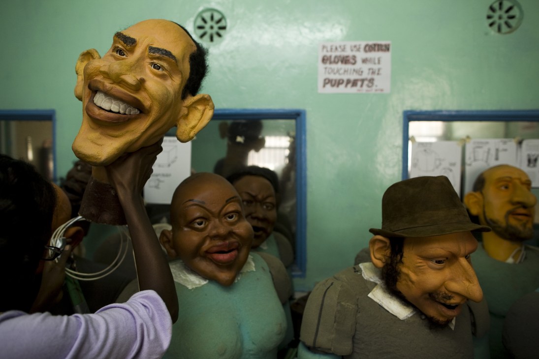 Collection of caricature puppets displayed in a studio workshop with a sign requesting gloves while handling.