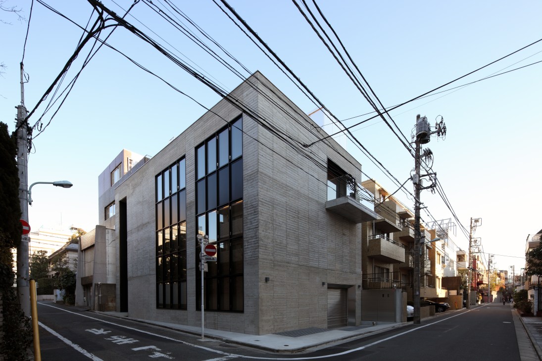 Concrete four-storey building with large windows on a Tokyo street corner at dusk.