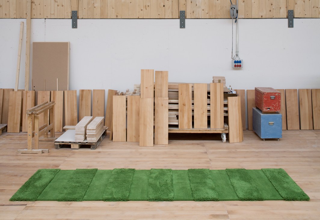 Green striped hand-tufted Balance rug by Kramis displayed in workshop with wooden frames and tools.