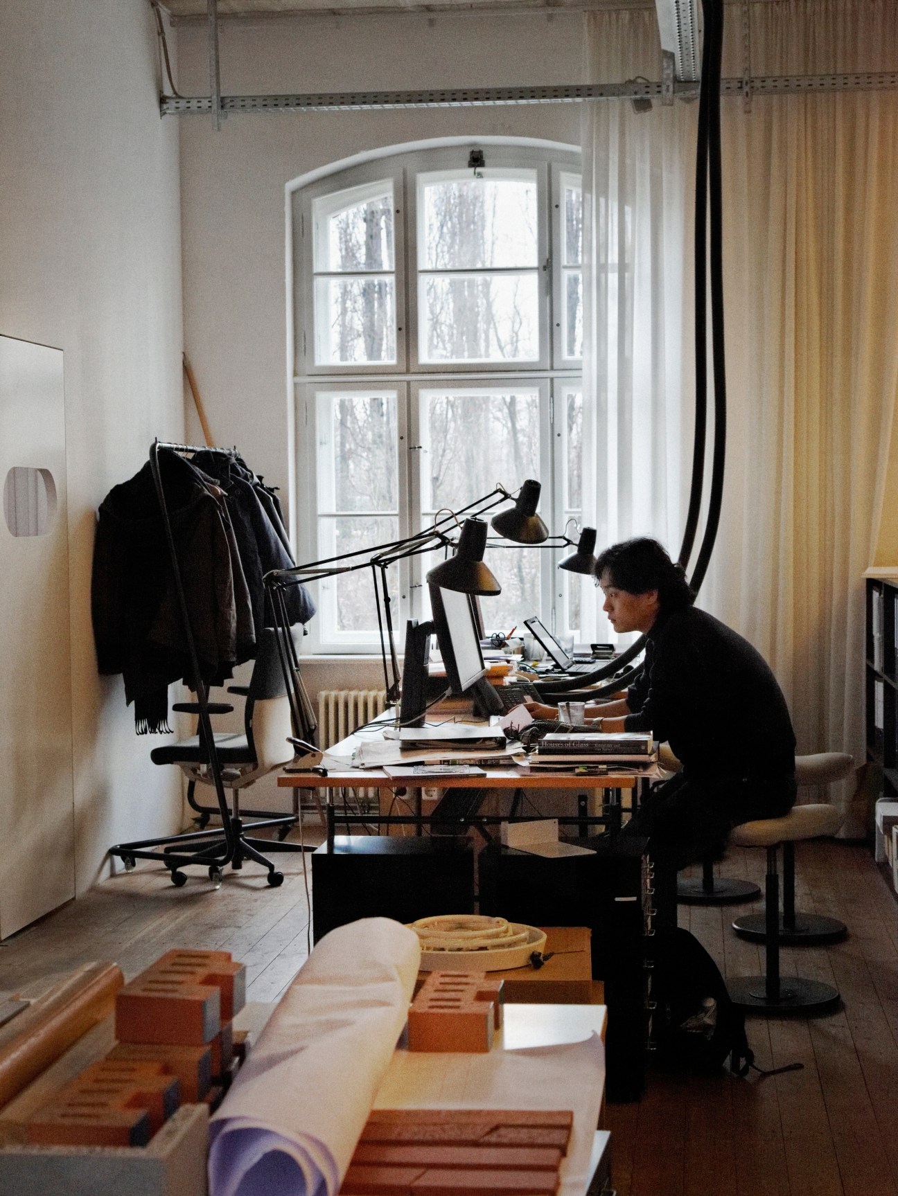 Intern Jiachen Zhang works at a desk in a bright studio space with large windows overlooking bare trees.