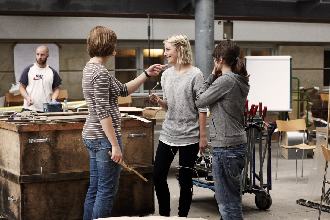 Students collaborate in a workshop at the Danish Design School with workbenches and tools visible.
