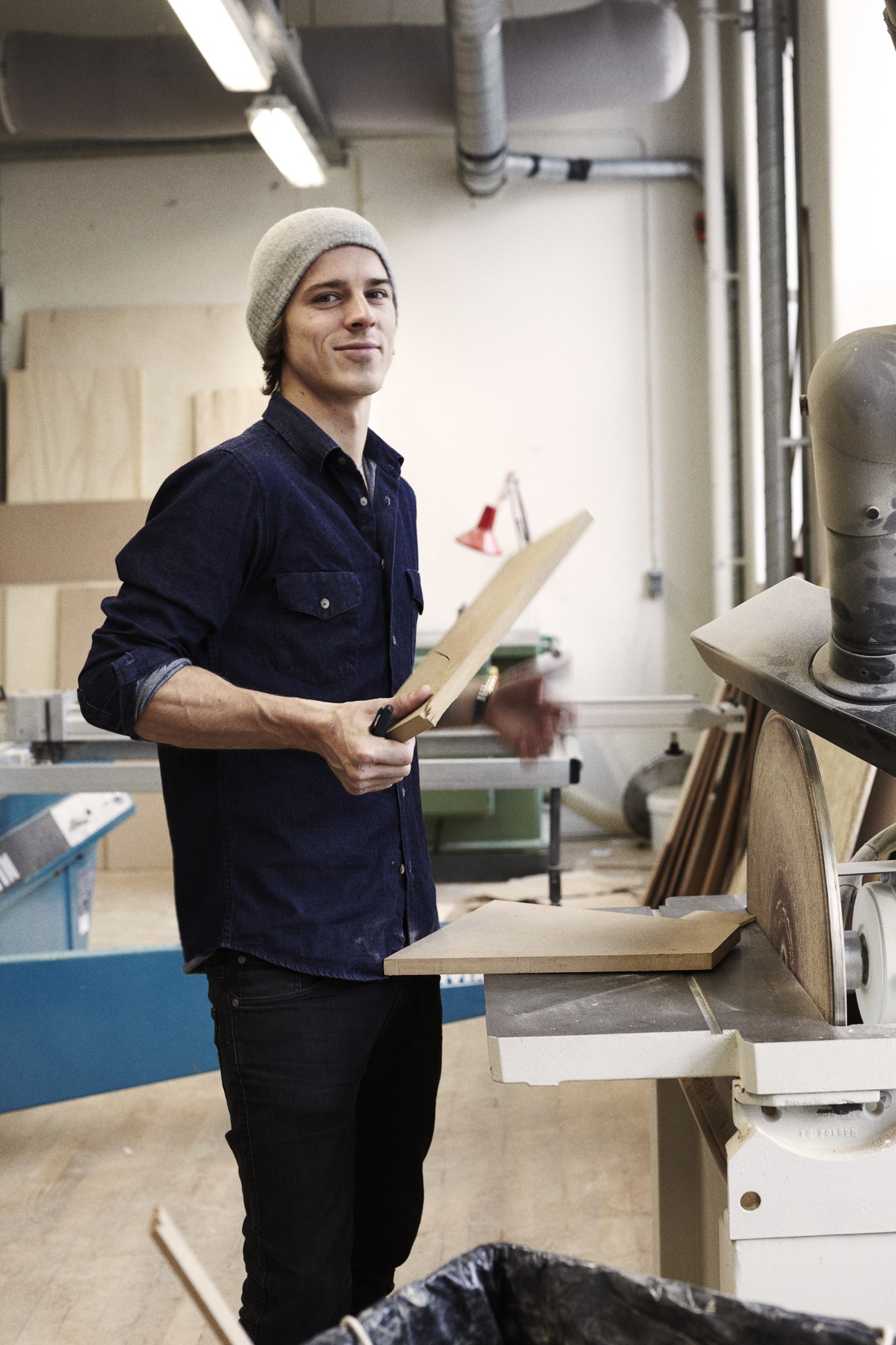 Young man in navy shirt and beanie working with wood in a workshop setting.