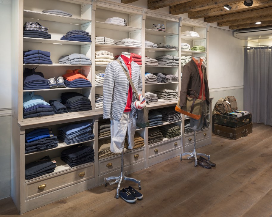 Interior of Biliardo boutique in Mirano showing organized shelving with folded clothing and a mannequin displaying a striped shirt with red scarf.