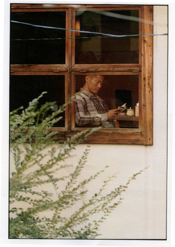 Man wearing a Hugo Boss shirt looking at his phone through a wooden window frame.