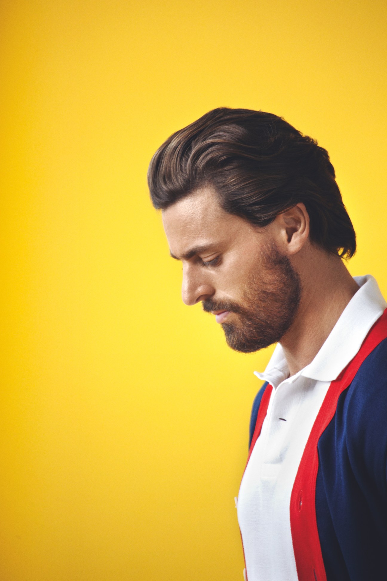 Man wearing Letroyes cardigan and Lacoste polo shirt against yellow background.