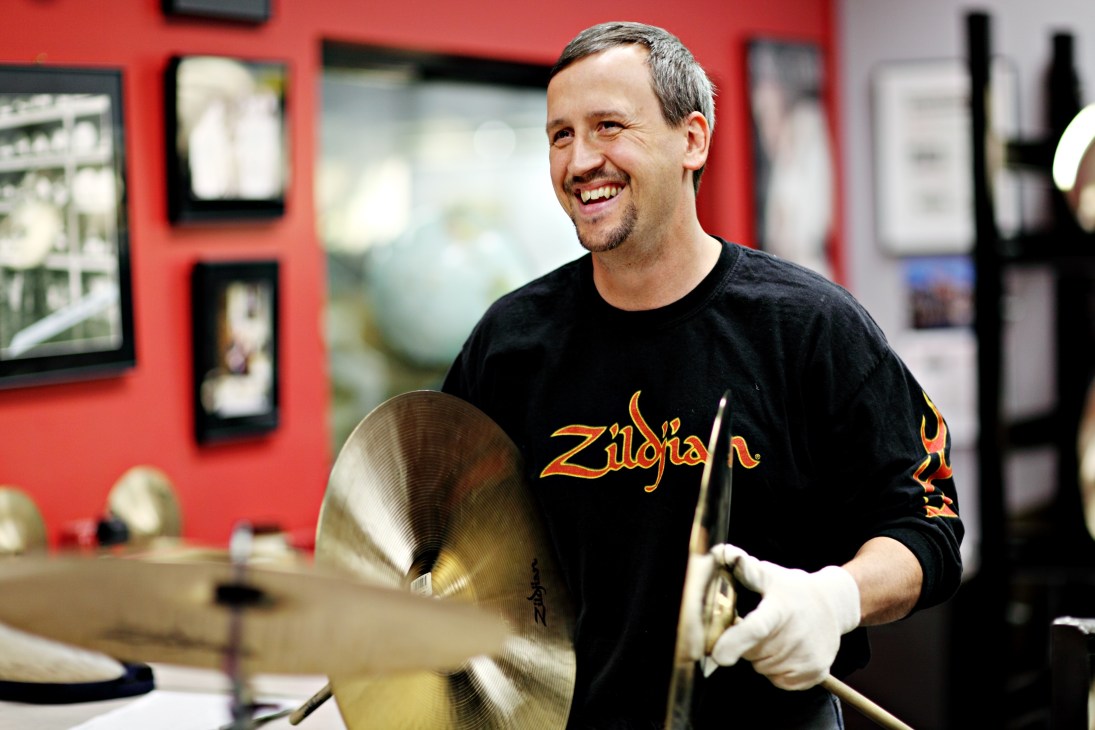 Jeff Westhaver smiles while holding cymbals in Zildjian's sound testing room with red walls.