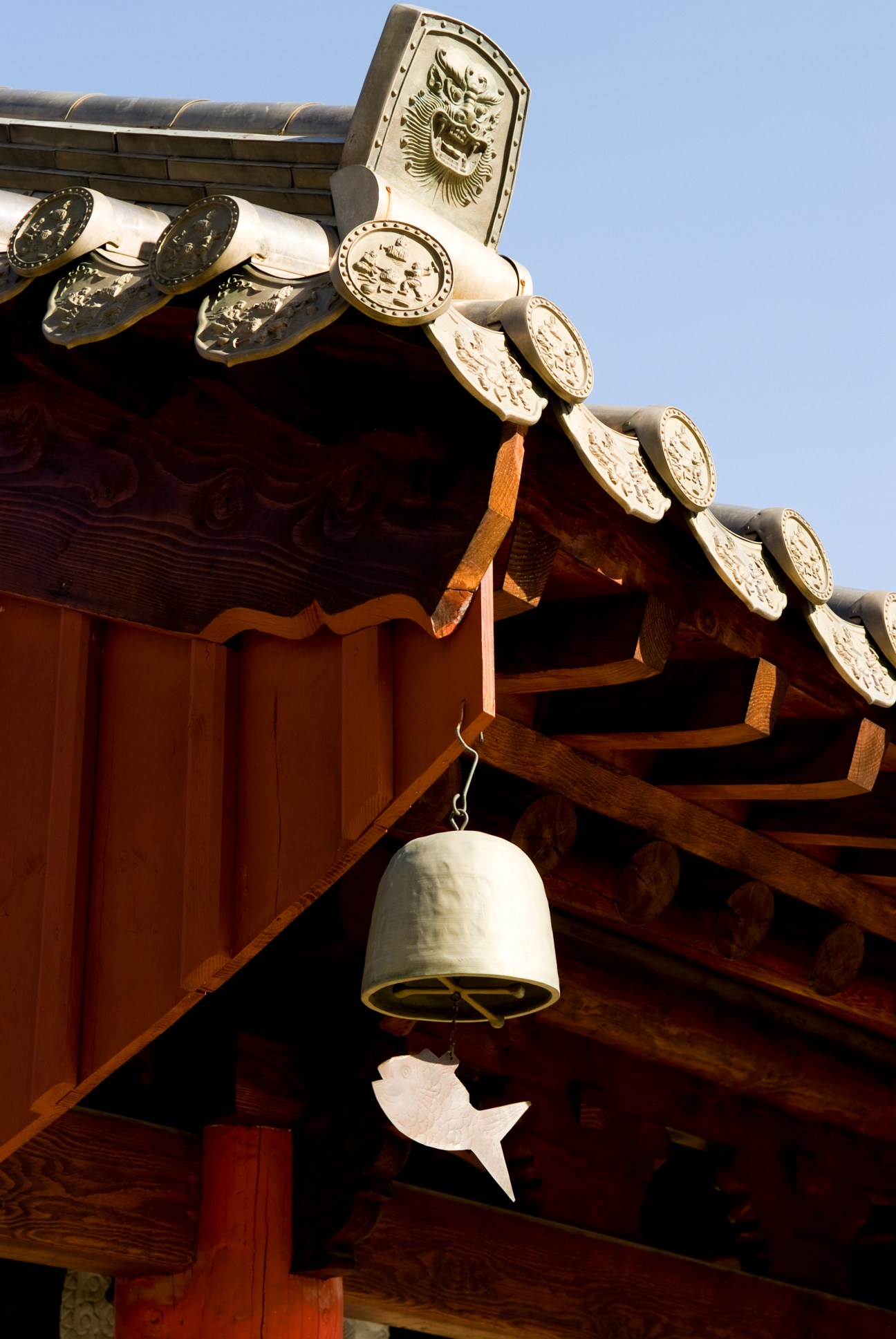 Traditional Korean temple roof with ornate bronze tiles and a hanging bell with leaf-shaped clapper.