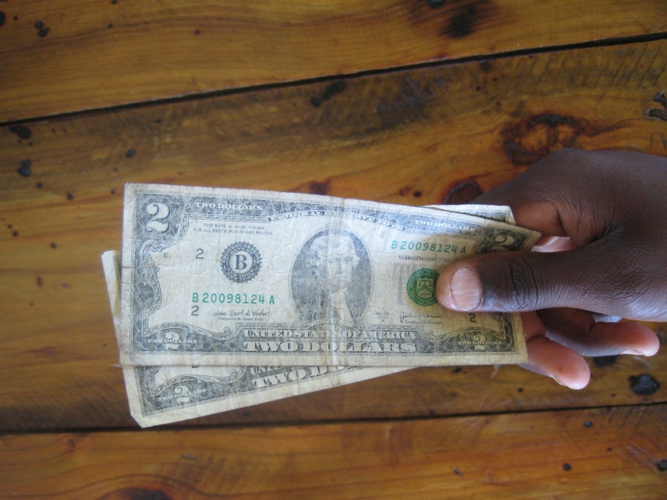 Hand holding US $2 bills over a wooden surface.