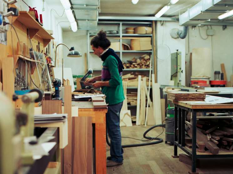 Craftsperson working at a wooden workbench in a model-making workshop filled with tools and materials.