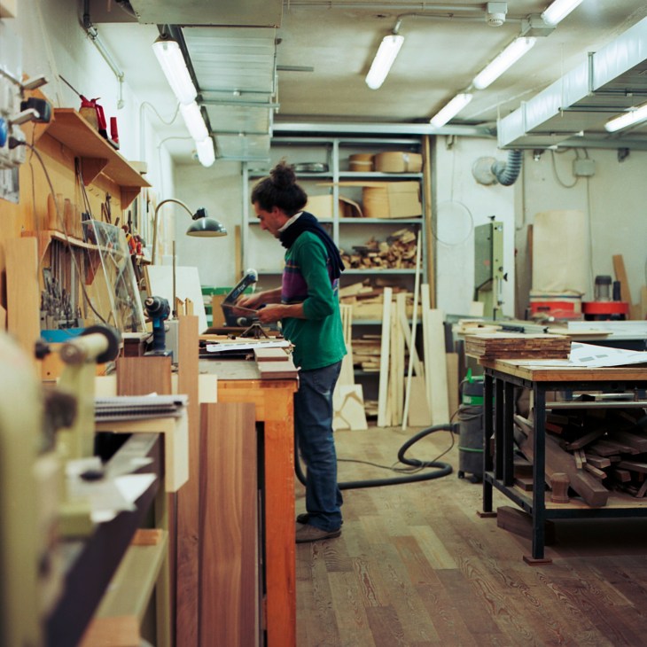 Craftsperson working at a wooden workbench in a model-making workshop filled with tools and materials.
