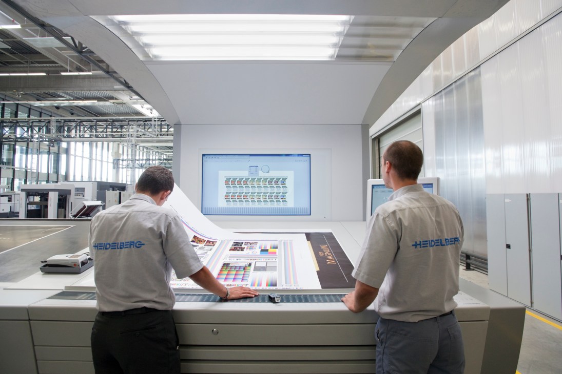 Two Heidelberg technicians examine print color samples at a quality control station.
