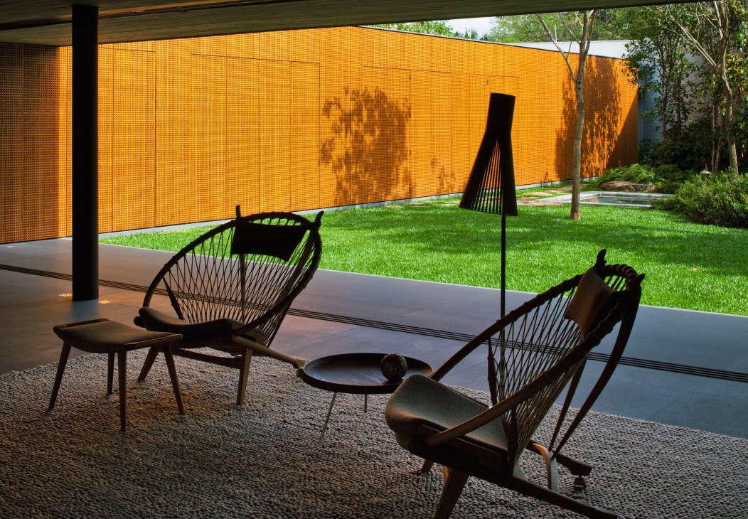 Two Hans Wegner Circle Chairs with black frames positioned on a concrete floor facing a yellow perforated metal wall and garden beyond.
