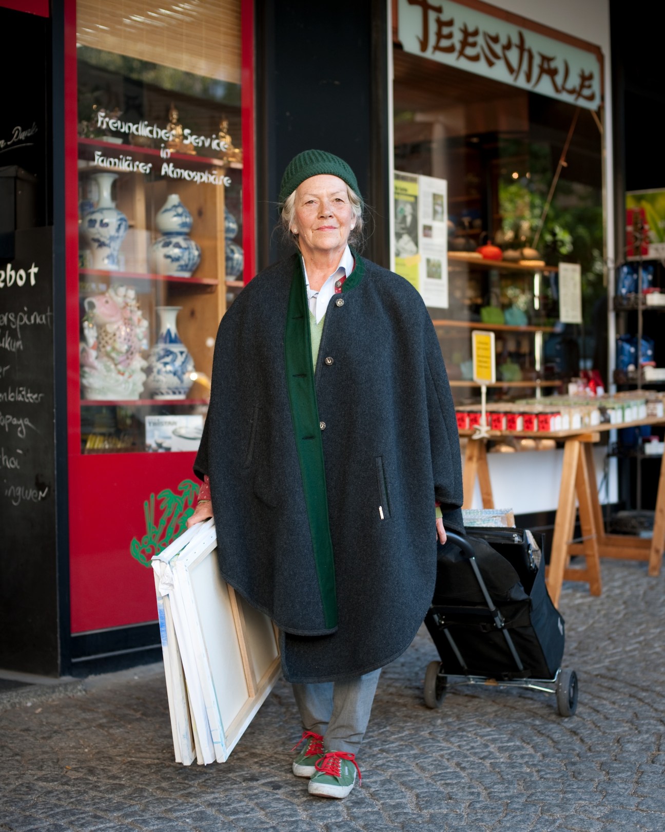 Painter Veronika Hilka stands outside a shop at Viktualienmarkt wearing a dark coat and green beanie.