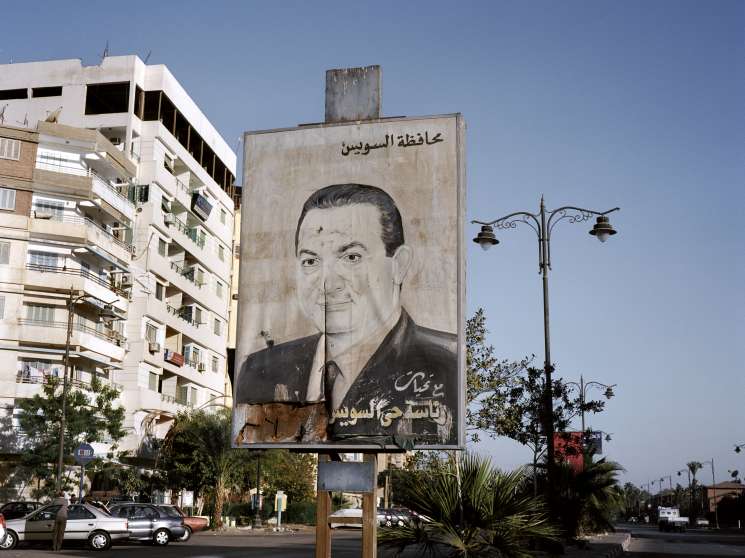 A large weathered billboard portrait of Hosni Mubarak in Port Fouad, Egypt, with Arabic text above and below.