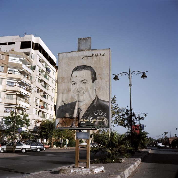 A large weathered billboard portrait of Hosni Mubarak in Port Fouad, Egypt, with Arabic text above and below.