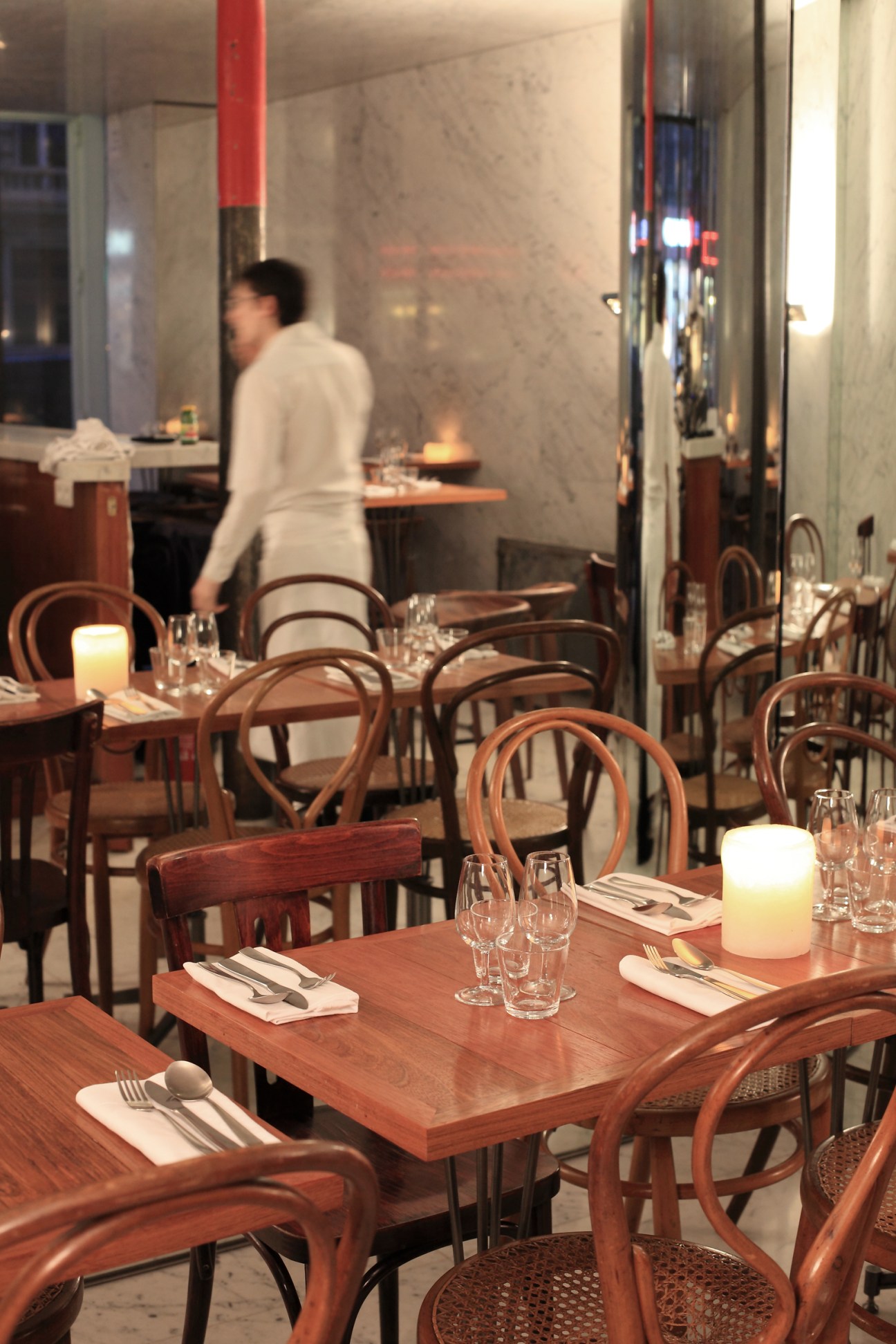 Modern dining room at Le Dauphin restaurant with wooden chairs, set tables with candles, and mirrored walls.