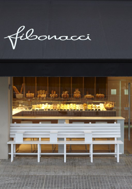 Fibonacci bakery storefront in Mallorca with illuminated display window of baked goods and white bench seating.
