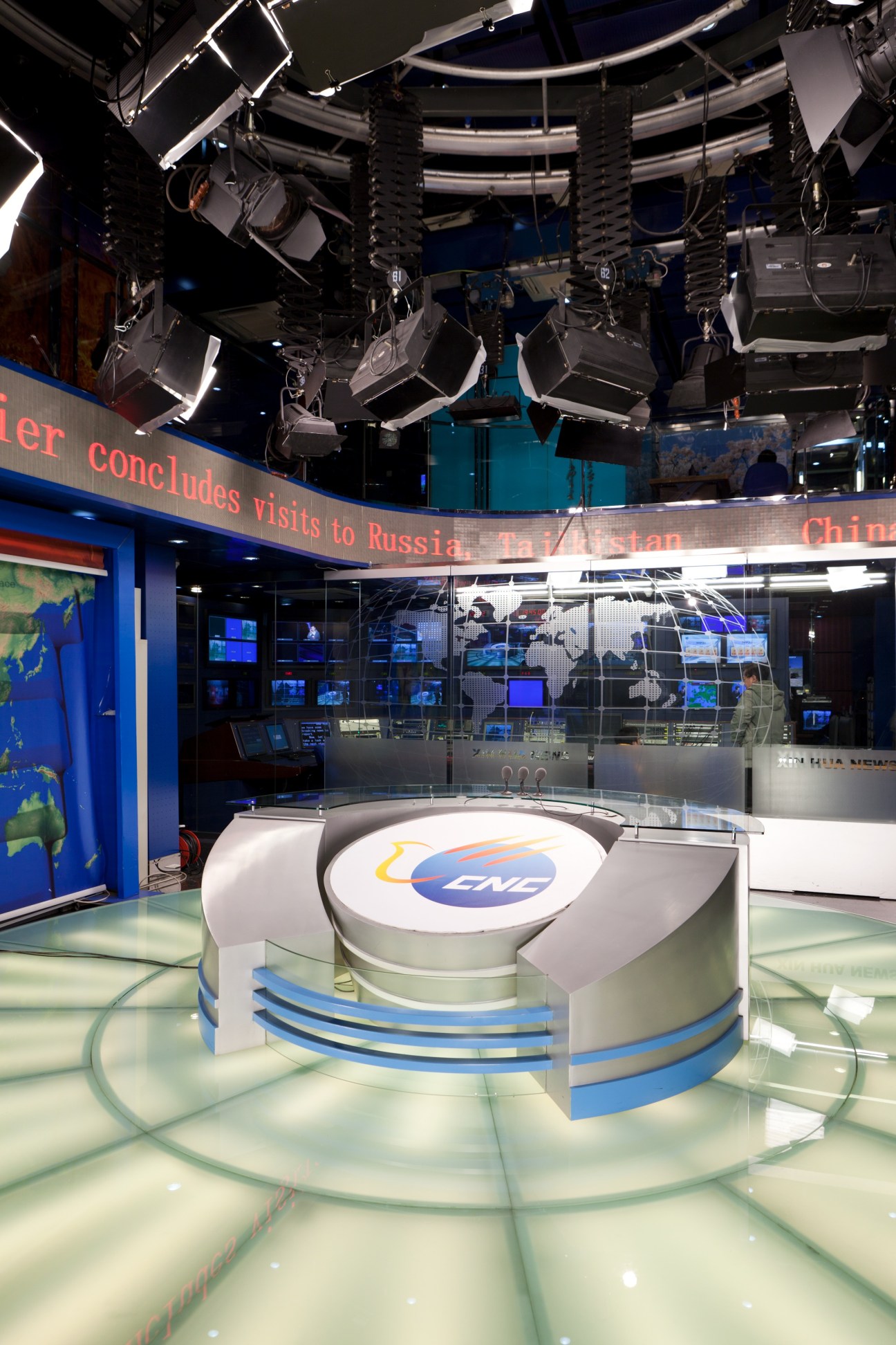 CNC World television studio anchor desk with logo, surrounded by professional lighting and control room equipment.