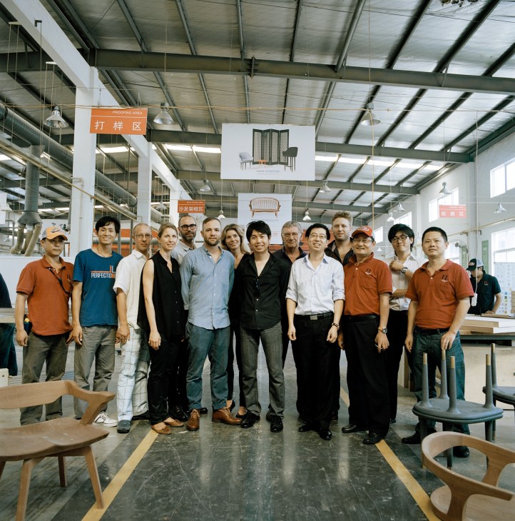 Stellar Works team posing together inside Furniture Labo factory with wooden furniture and bilingual signage visible.