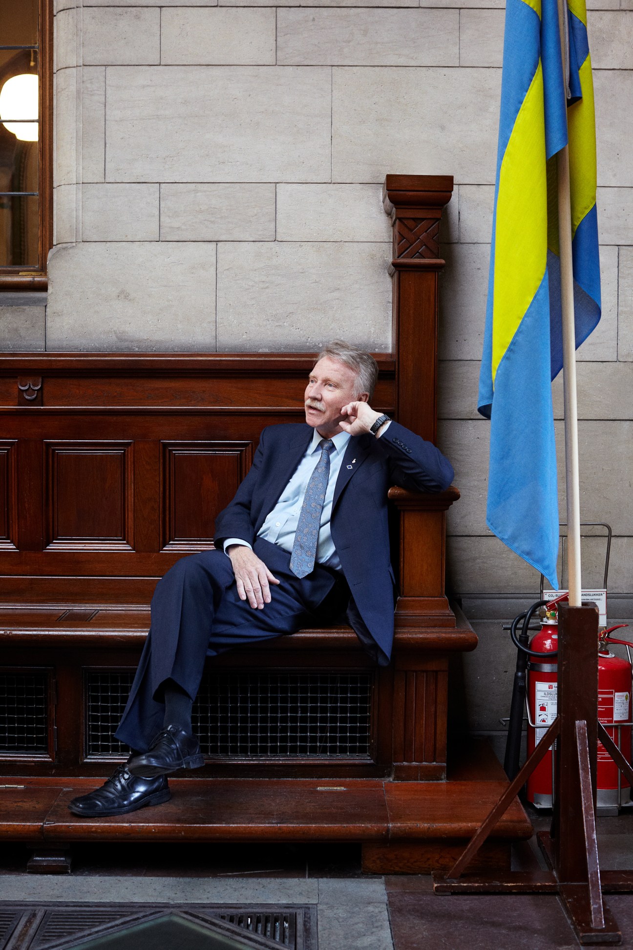 Ilmar Reepalu, mayor of Malmö, sits on a wooden bench inside Copenhagen town hall next to Swedish flags.