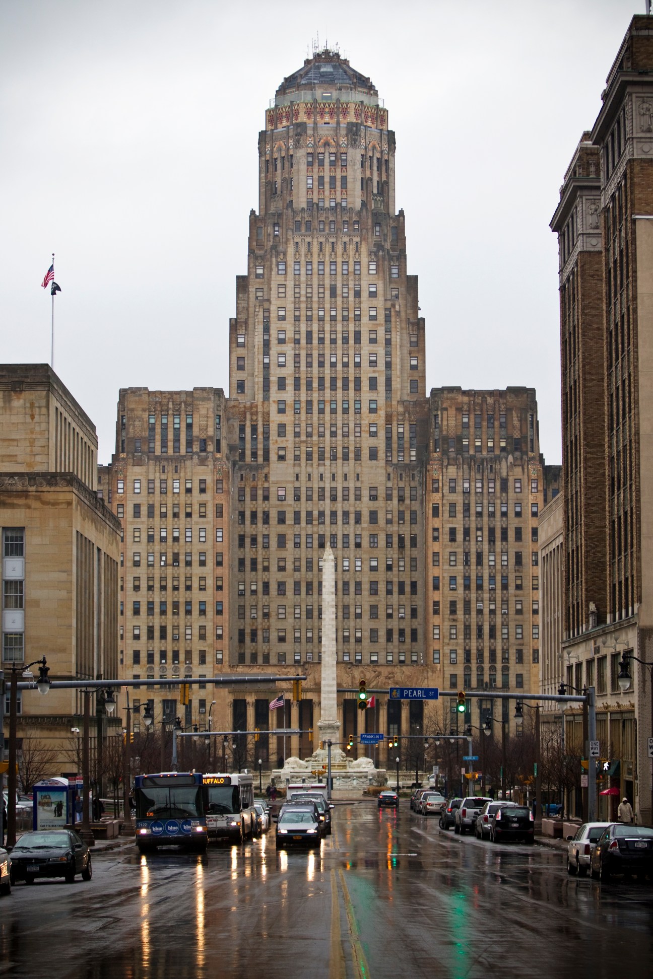 Buffalo City Hall, a tall Art Deco building with ornate crown, dominates a wet city street lined with classical architecture.