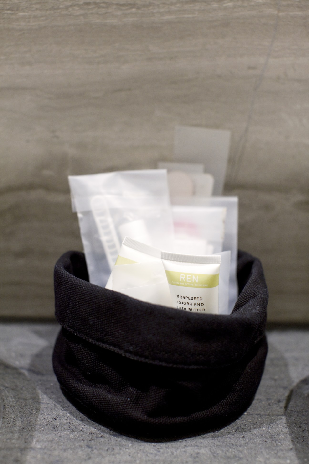 Skincare product packets with REN branding arranged in a black pouch on concrete.