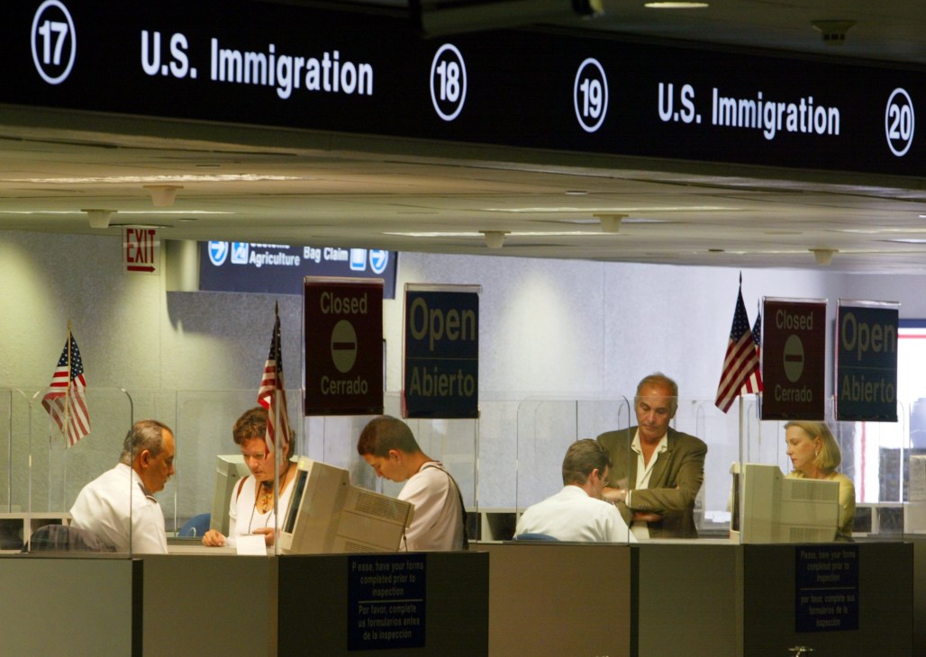 US Immigration counter with officials and visitors at an airport or border crossing facility.