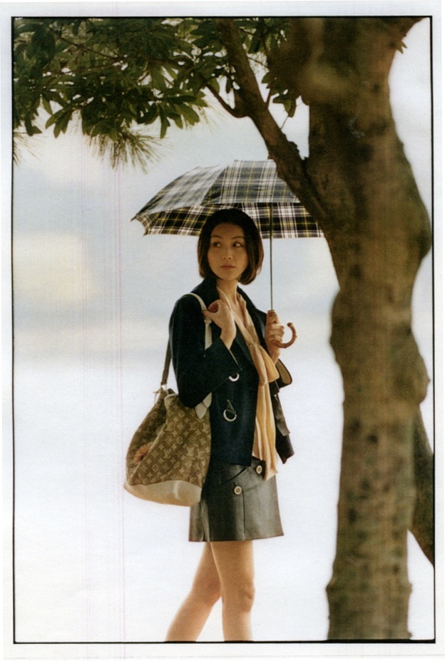 Woman holding a plaid umbrella under a tree wearing a Louis Vuitton jacket and skirt with Chloé blouse