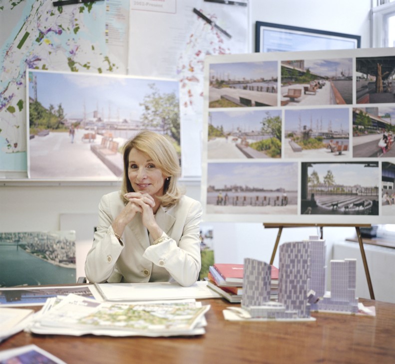 Amanda Burden, NYC planning commissioner, sitting at her desk surrounded by architectural renderings and urban design sketches.