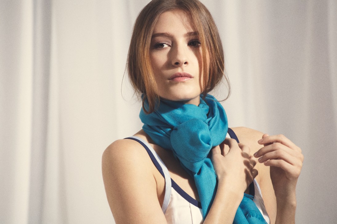 Woman wearing a turquoise Begg scarf, made from light cashmere and silk-blend fabrics.