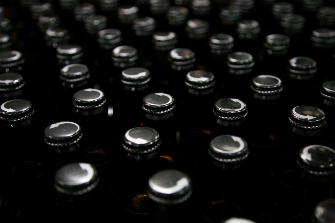 Close-up of metal bottle caps on dark glass beer bottles.