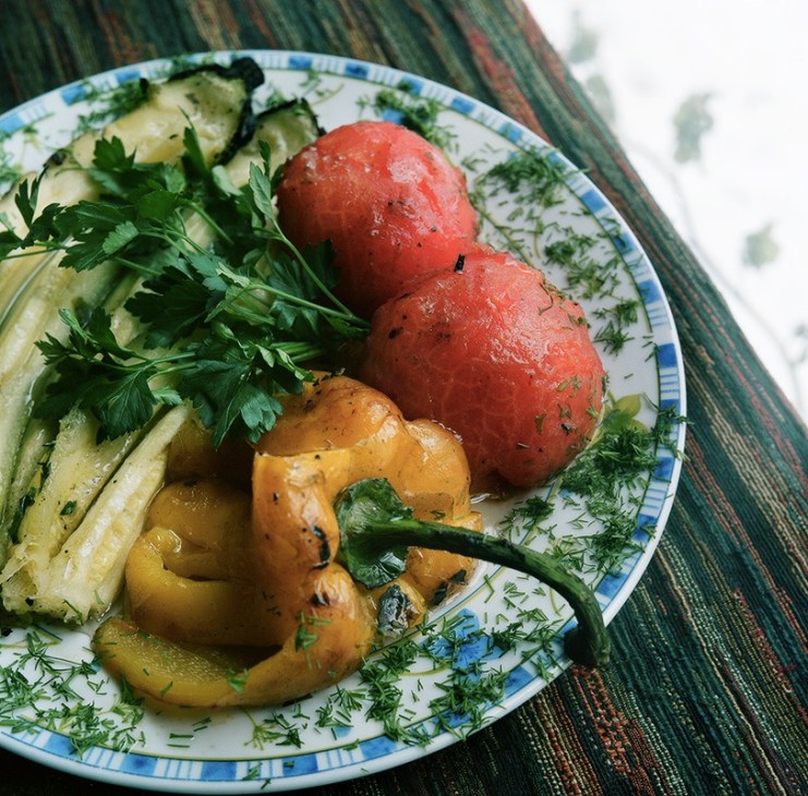 Grilled vegetables on a decorative plate including tomatoes, peppers, zucchini and fresh parsley.