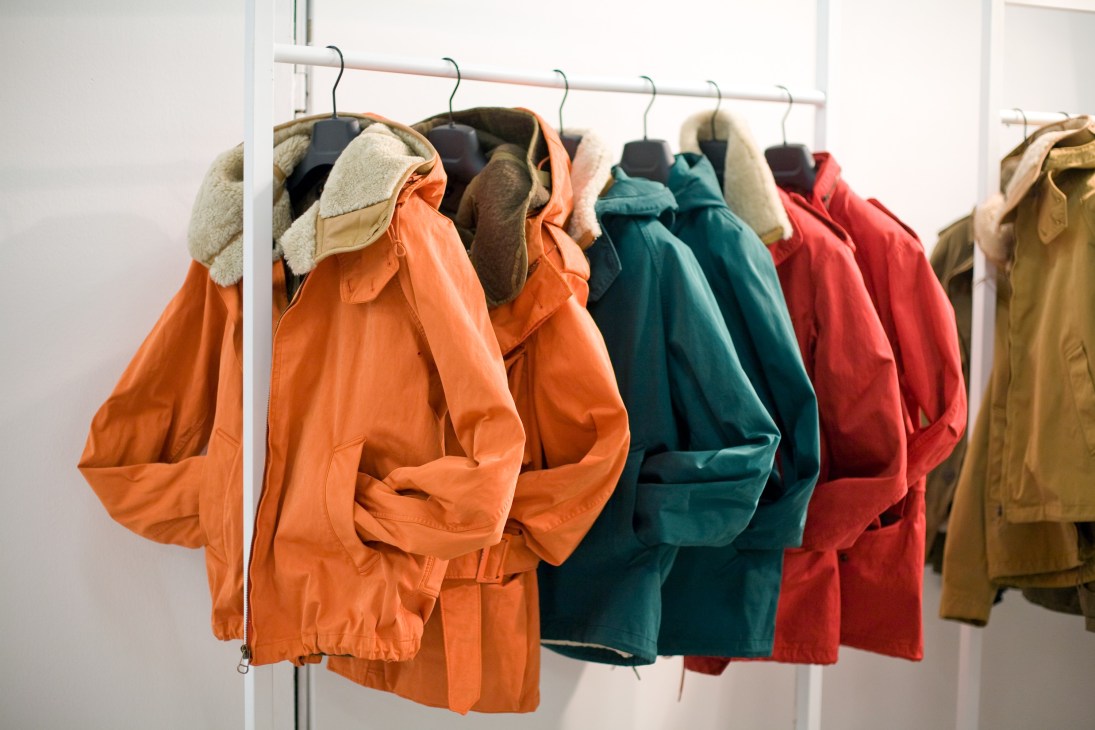 Colorful padded jackets with sherpa lining hung on a metal rail, including orange, teal, red and olive styles.